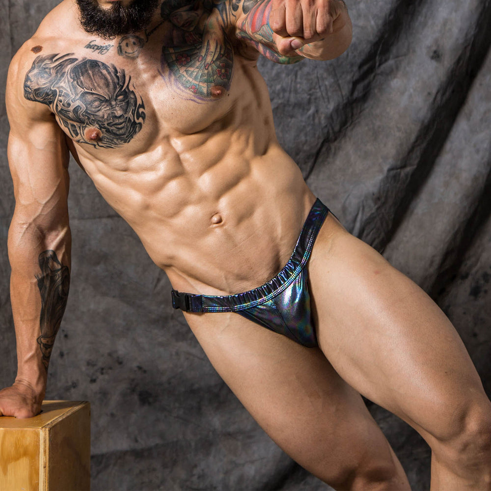Person wearing iridescent black buckle-front swim briefs against a dark backdrop