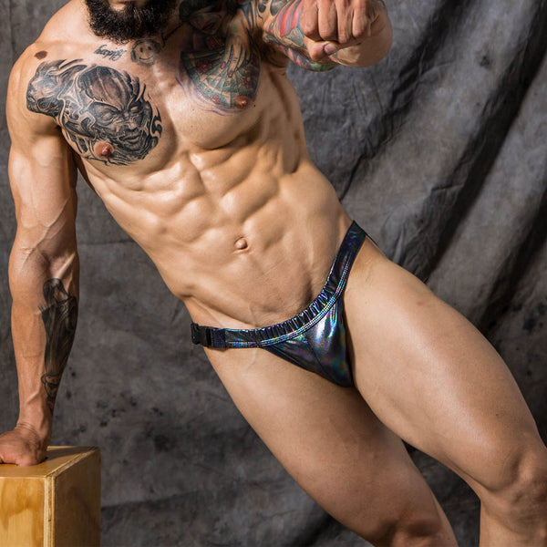 Person wearing iridescent black buckle-front swim briefs against a dark backdrop