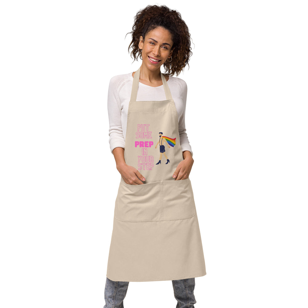 Front view of a model wearing a beige apron reading “PUT SOME PREP IN YOUR STEP” with a rainbow-caped figure