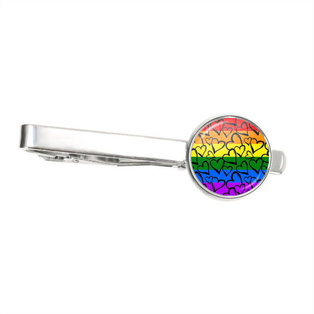 Silver tie clip with a round rainbow heart-patterned face, shown on white