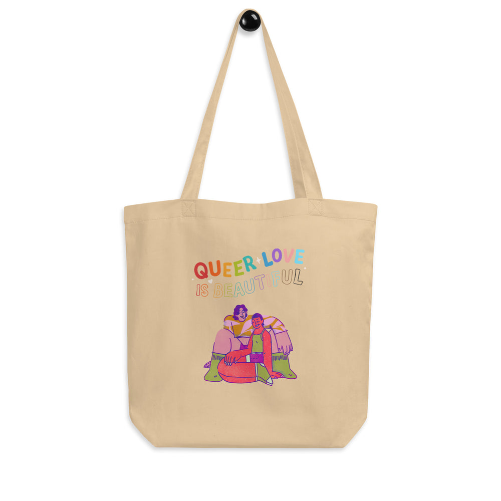 Natural canvas tote bag reading “QUEER LOVE IS BEAUTIFUL,” with an illustration of two people seated together
