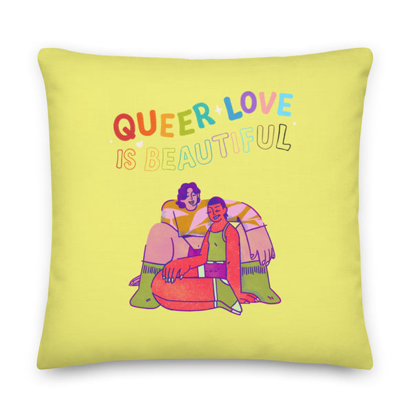 Square yellow pillow reading “QUEER LOVE IS BEAUTIFUL,” with two people embracing