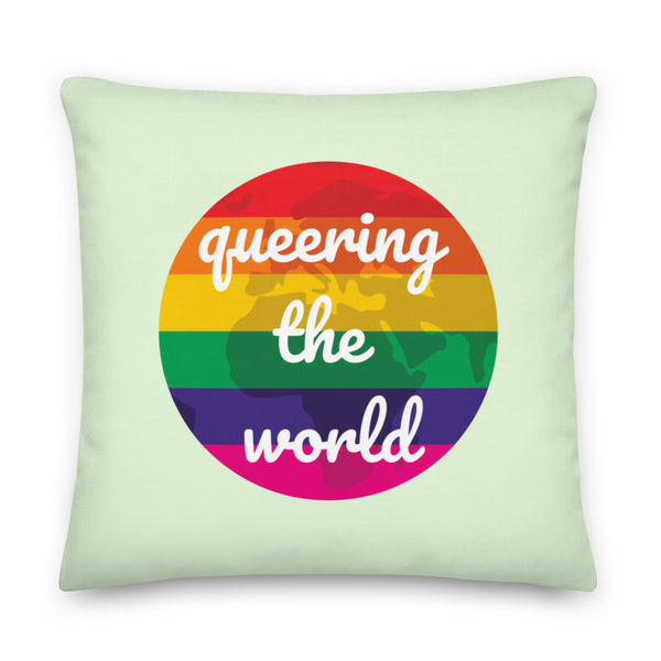 Front-facing pale green pillow with a rainbow globe graphic and white “queering the world” text