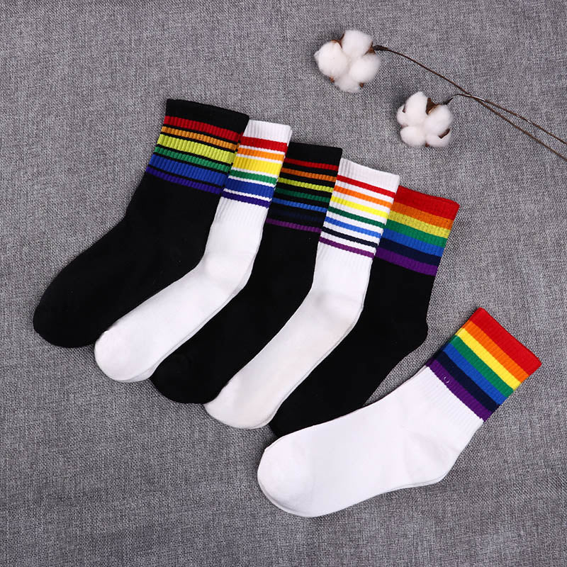 Five black and white socks with rainbow-striped cuffs arranged on gray fabric