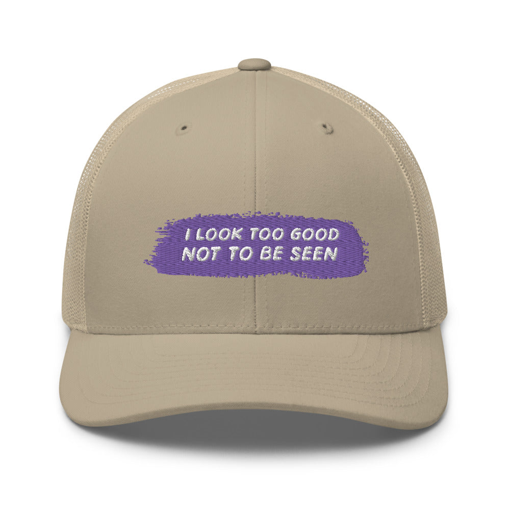 Front view of a beige trucker cap with purple patch reading “I LOOK TOO GOOD NOT TO BE SEEN”