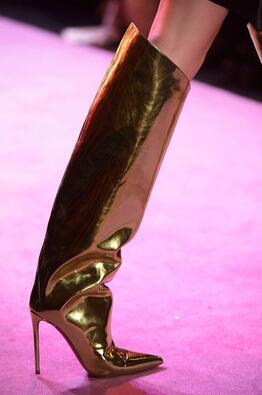 Close-up of a metallic gold thigh-high stiletto boot on a pink-lit runway