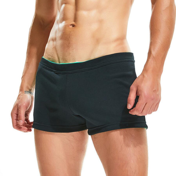 Front view of a shirtless model wearing black fitted workout shorts with green trim