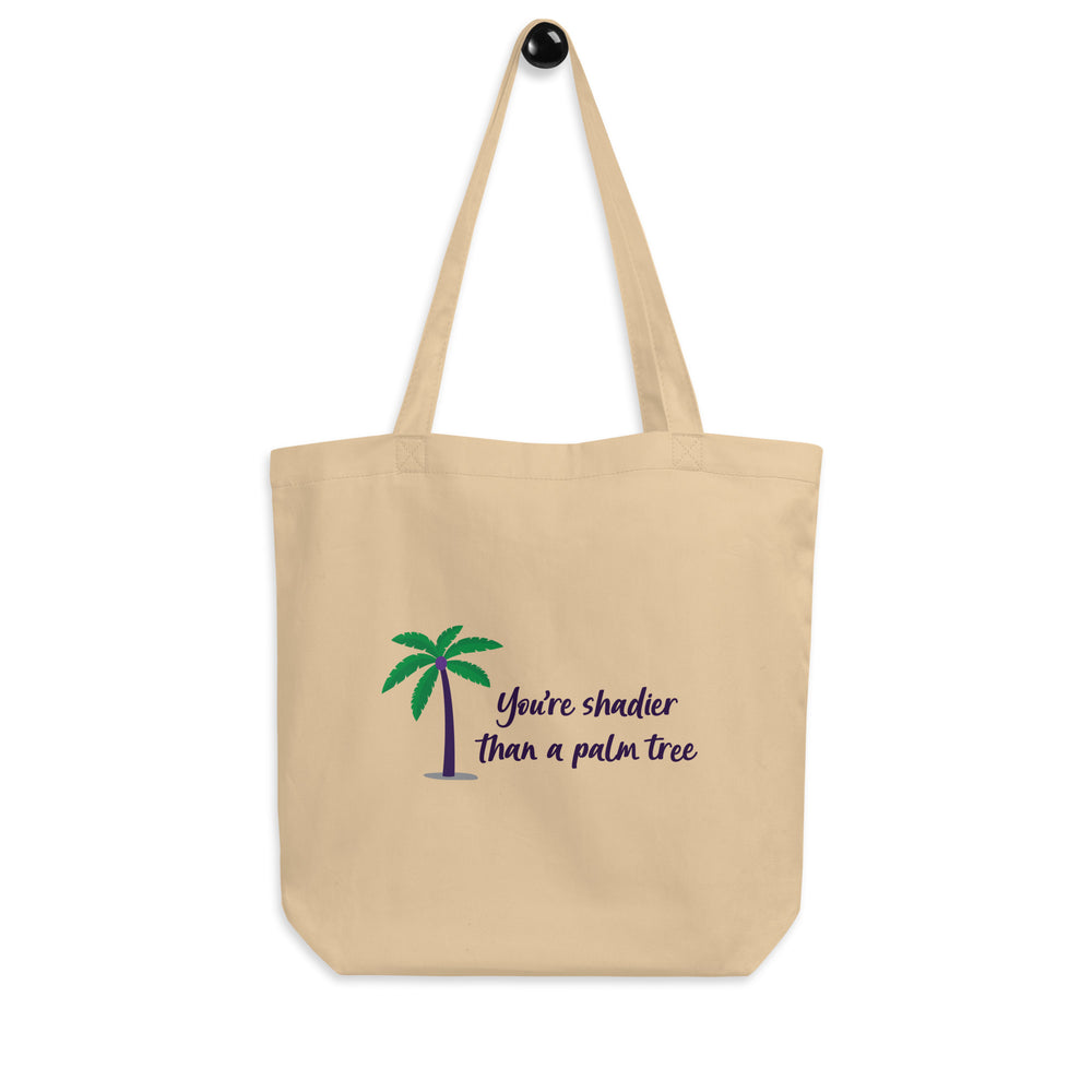 Front-facing beige tote bag with a palm tree and the words “You’re shadier than a palm tree.”