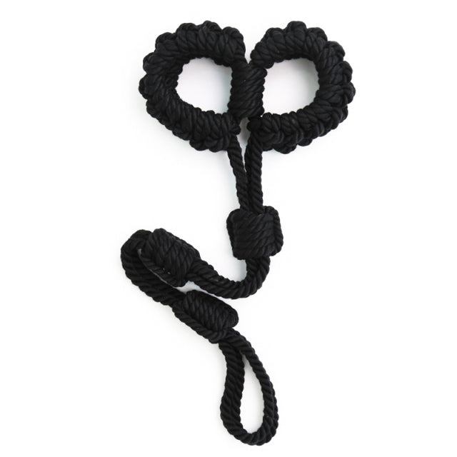 Black braided rope shibari handcuffs arranged in a heart-like shape on white