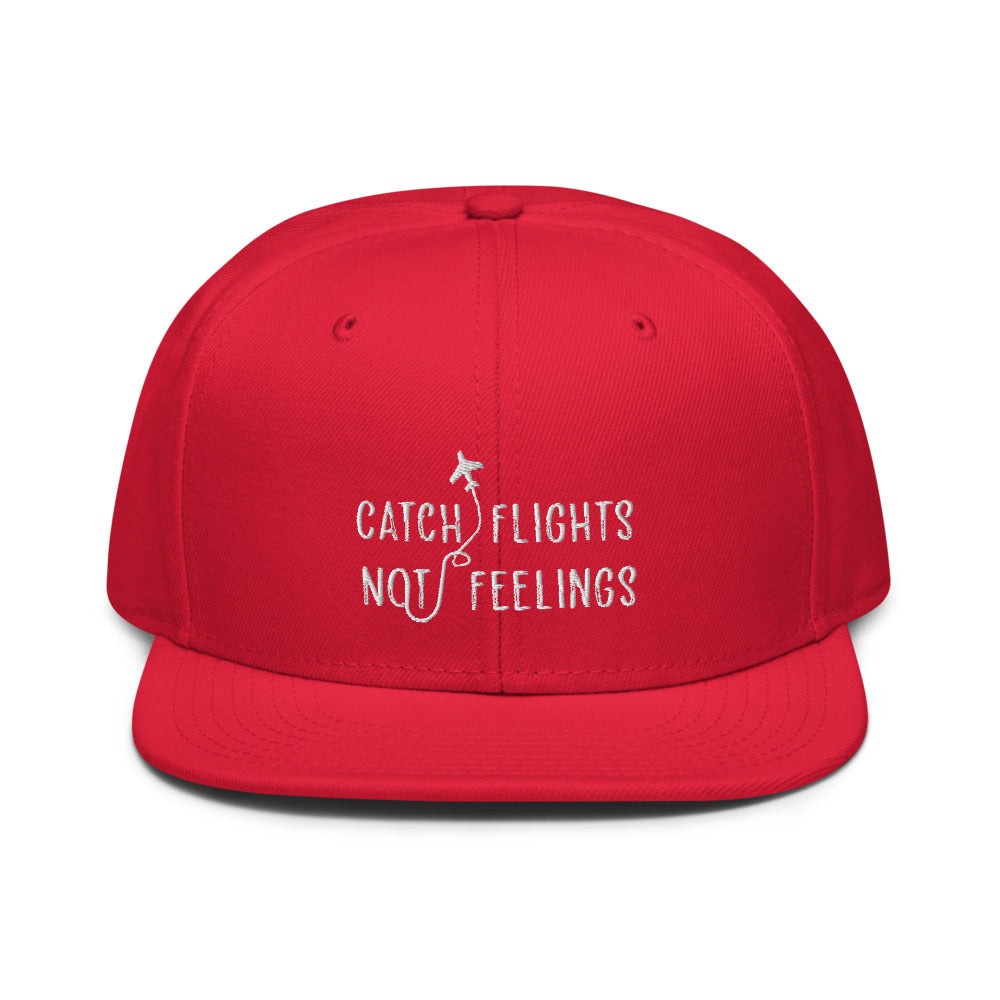 The "Catch Flights Not Feelings" Snapback Hat tops a glam person in pilot's drag, full beat and earrings, cockpit lights glowing behind.