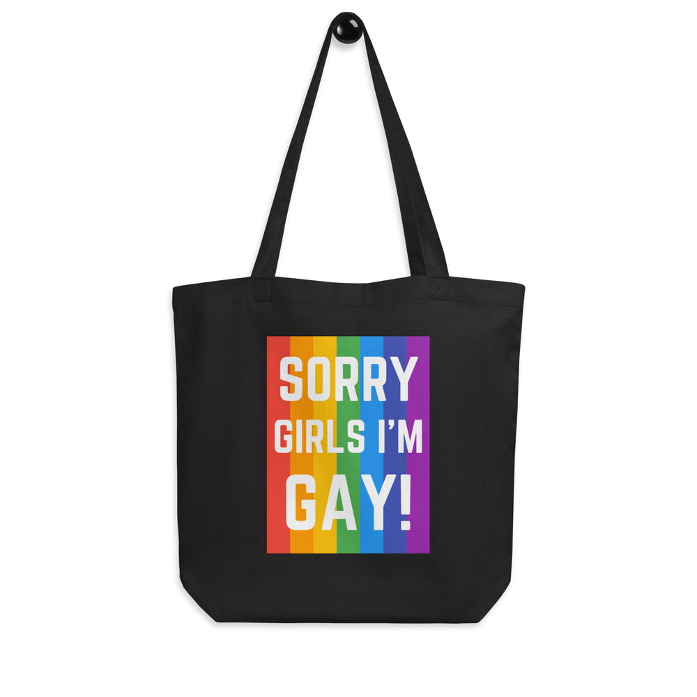 Front view of a black tote bag reading “SORRY GIRLS I’M GAY!” over rainbow stripes