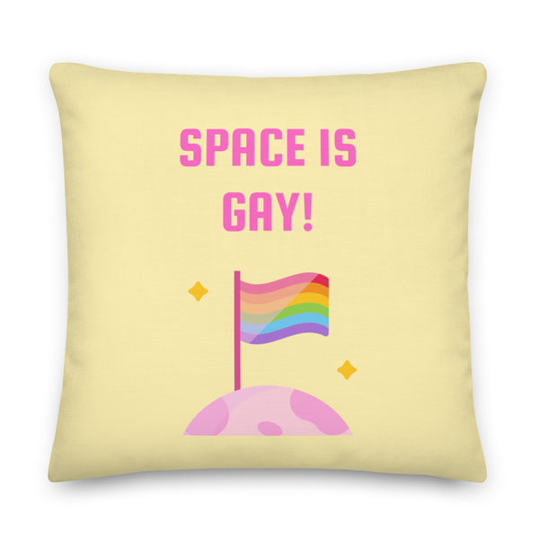 Pale yellow square pillow reading “SPACE IS GAY!” above a rainbow pride flag on a pink planet