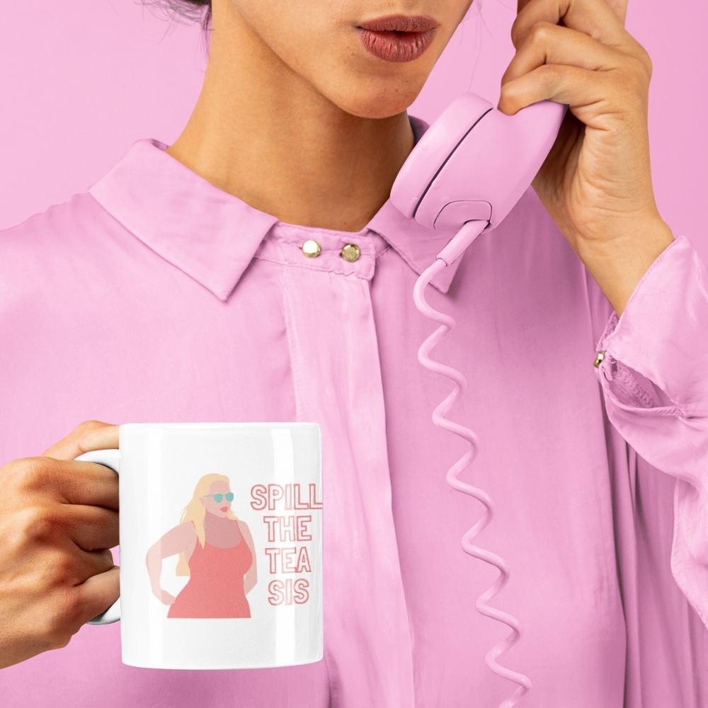 White gossip mug reading “SPILL THE TEA SIS” with a colorful illustrated figure, held by a person