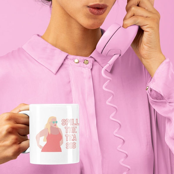 White gossip mug reading “SPILL THE TEA SIS” with a colorful illustrated figure, held by a person
