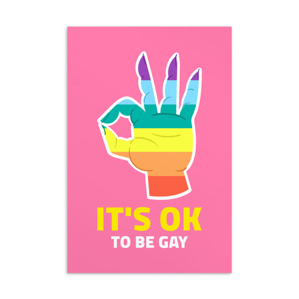 Pink postcard reading “IT’S OK TO BE GAY” beneath a rainbow-colored hand illustration