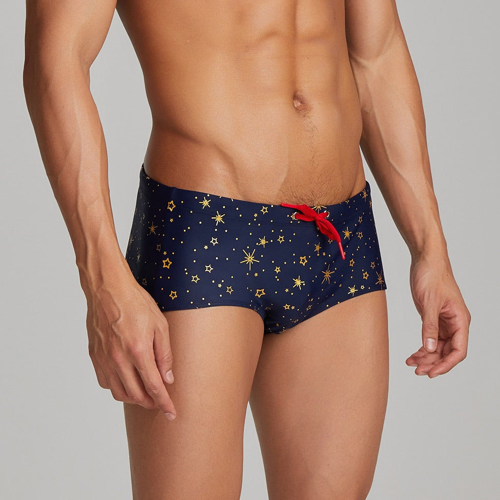 Cropped front view of a model wearing navy low-waist swim briefs with gold star patterns and a red drawstring