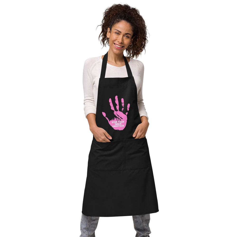 Front view of a model wearing a black apron with a pink handprint and “STOP YOUR INNER SABOTEUR” text