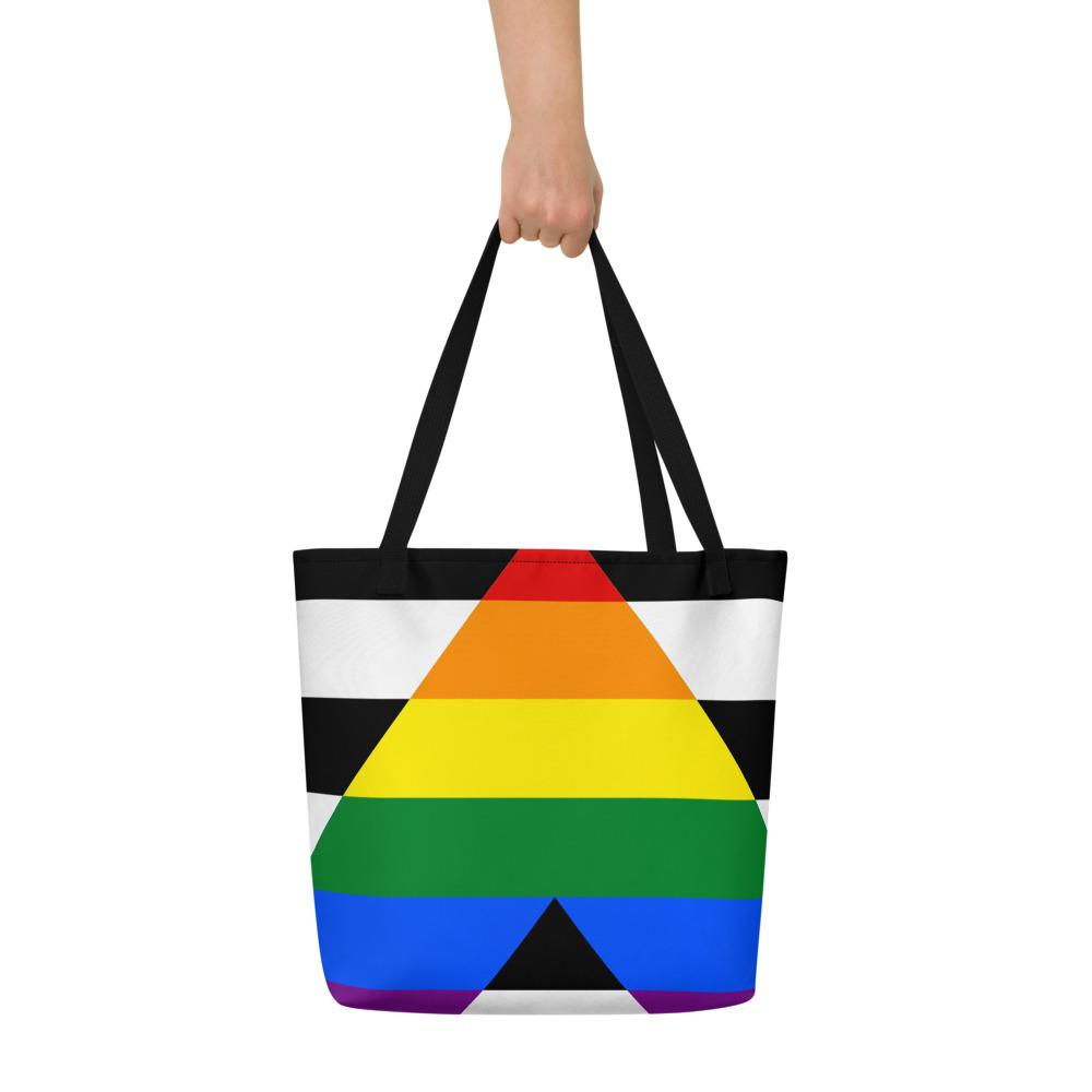 Black tote bag held by one hand, featuring a rainbow and black chevron-style stripes