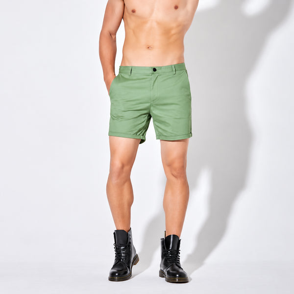 Front view of a shirtless model wearing sage-green chino shorts and black boots