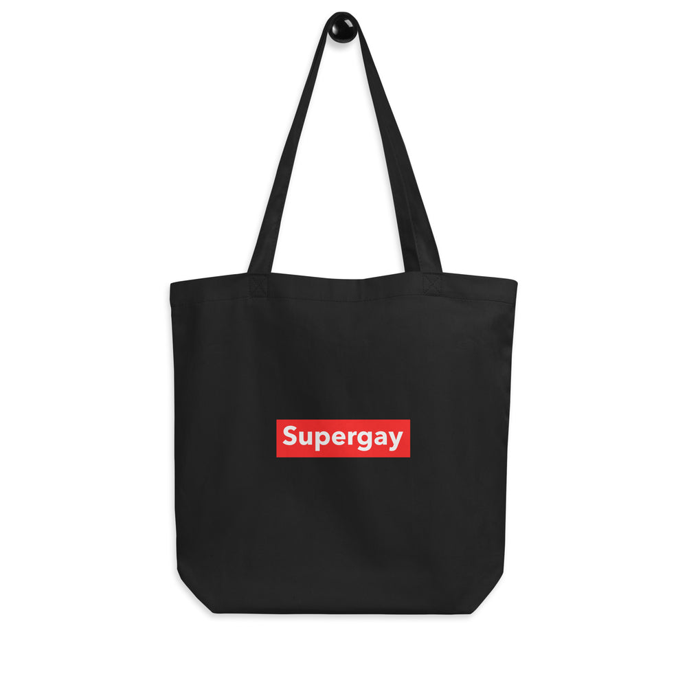Front view of a black tote bag with long handles and a red patch reading “Supergay.”