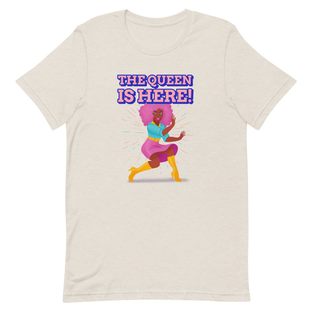 Front view of a light beige T-shirt reading “THE QUEEN IS HERE!” above a colorful dancing woman