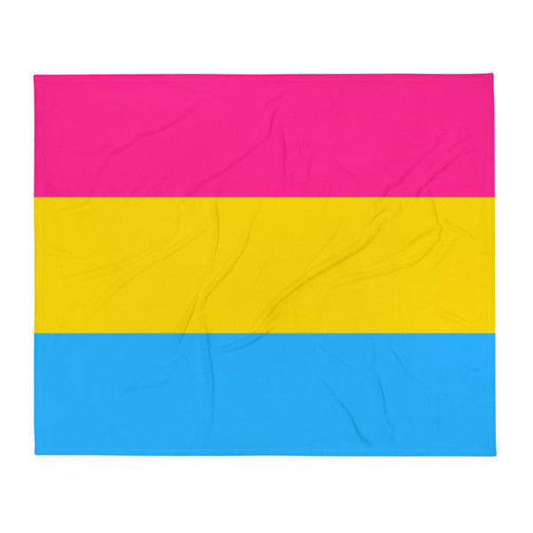 Pansexual Flag throw blanket with bold blue, yellow, and pink stripes wraps a smiling woman relaxing on a bed; soft room lighting.