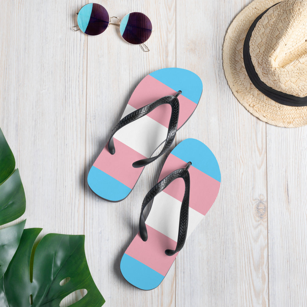 Transgender Pride flip-flops with pink, blue, and white striped soles and black straps