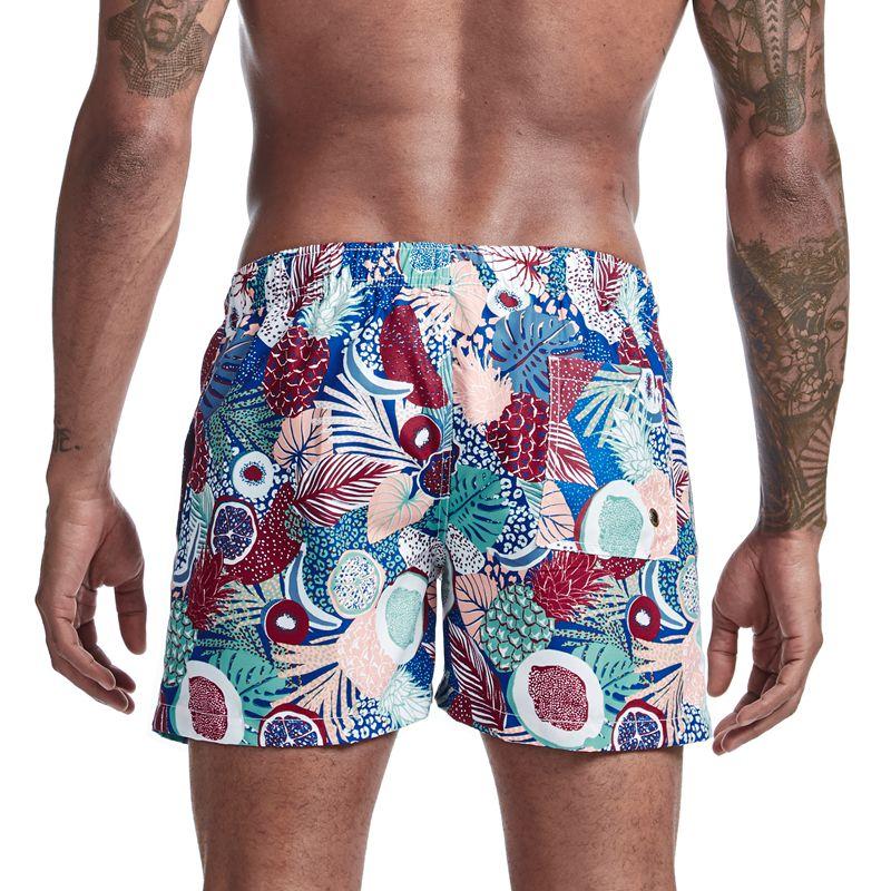 Rear view of a model wearing tropical-print board shorts with colorful leaves and fruit