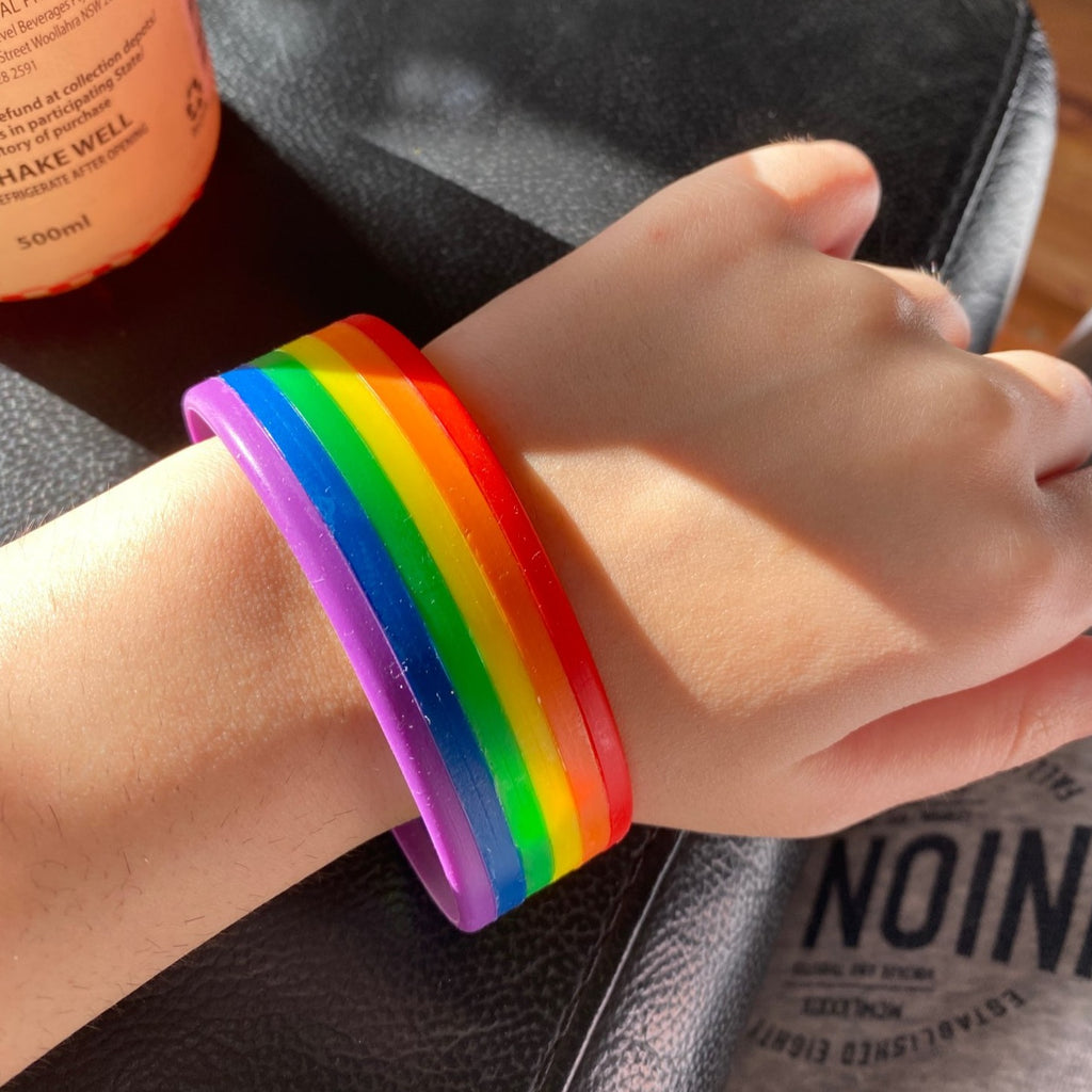 Close-up of a hand wearing a rainbow-striped rubber Pride wristband