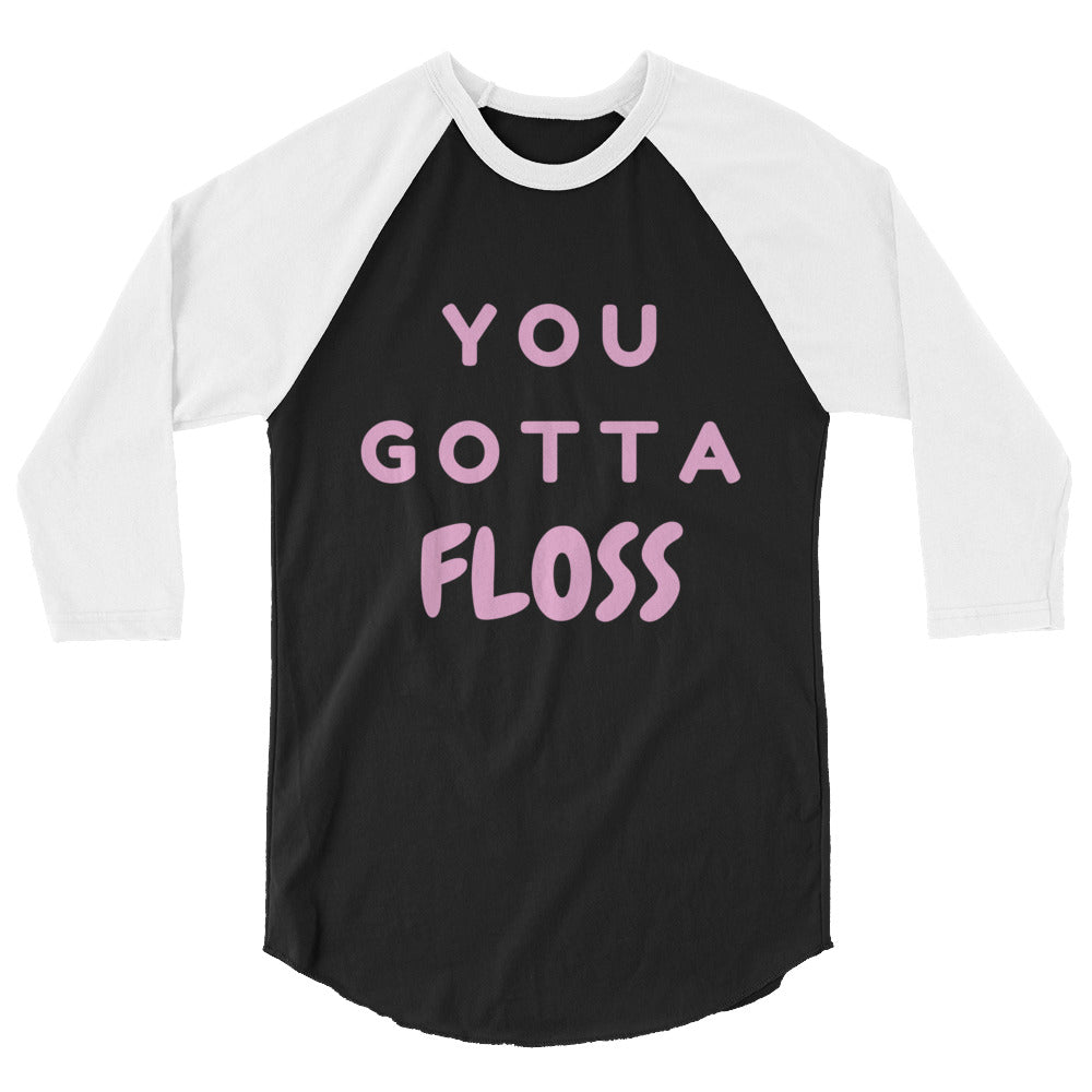 Front view of a black-and-white raglan shirt reading “YOU GOTTA FLOSS” in pink letters