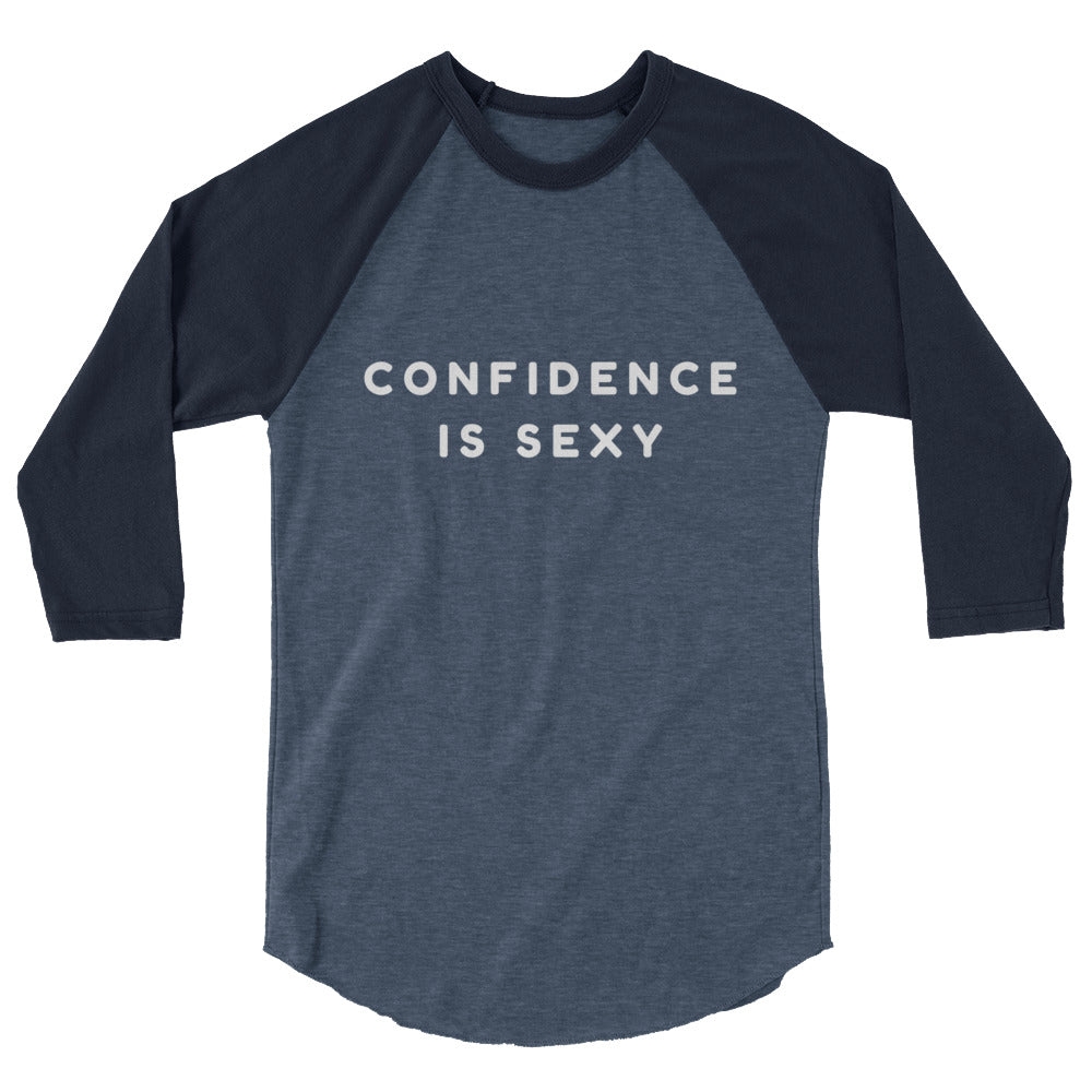 Confidence Is Sexy 3/4 Sleeve Raglan Shirt with bold “CONFIDENCE IS SEXY” print, worn by a queer person in jeans, serious gaze.