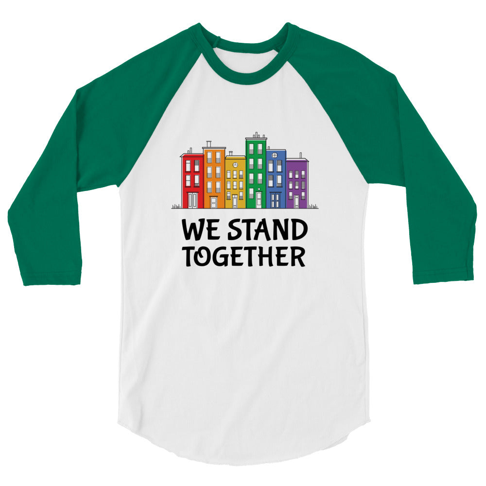 Front view of a white and green raglan shirt reading “WE STAND TOGETHER” beneath colorful buildings