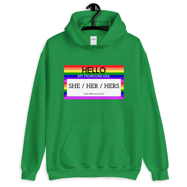 Green hoodie with rainbow-striped pronoun badge reading “HELLO MY PRONOUNS ARE: SHE / HER / HERS”