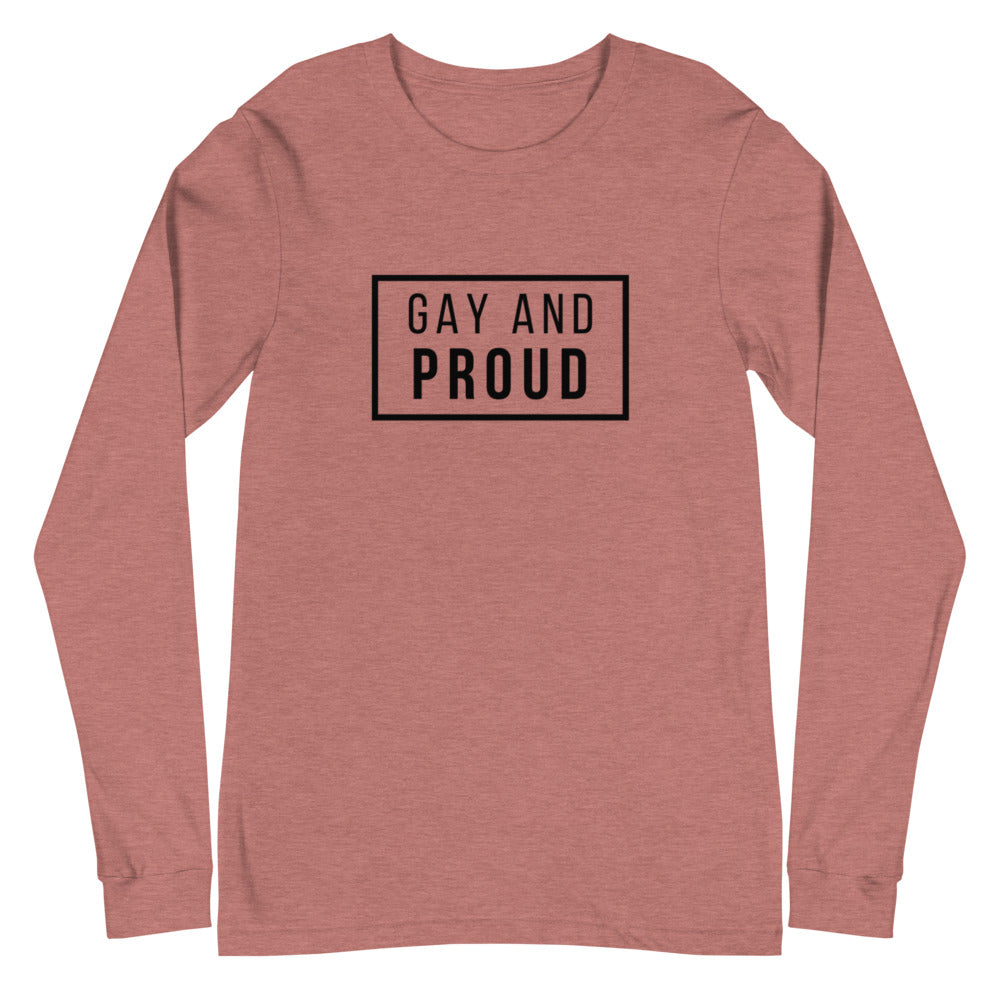 Gay And Proud Unisex Long Sleeve T-Shirt worn by a young man at dusk on a city street, tall buildings and blurred lights behind him.