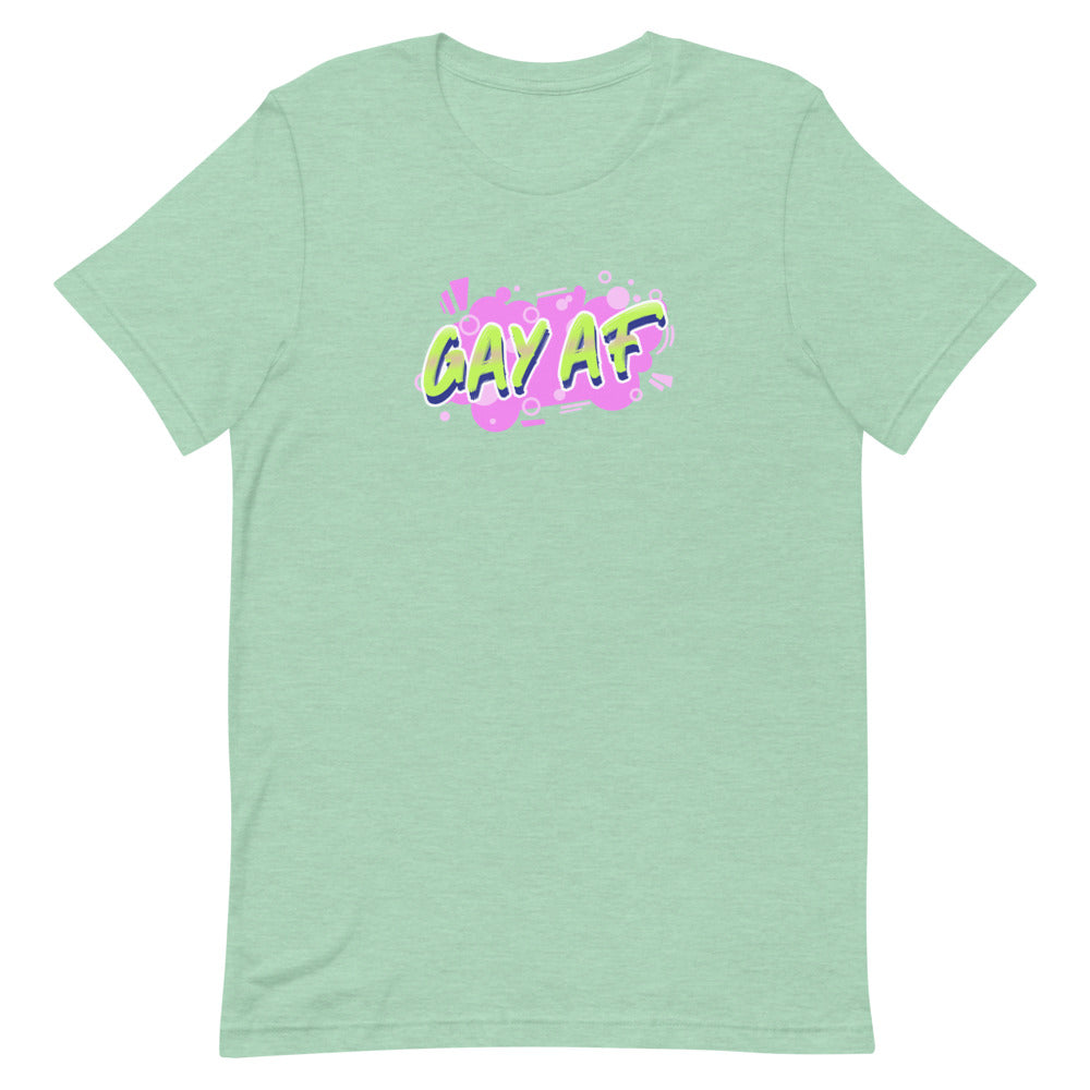 Unisex pale green pride tee with bold, colorful graffiti "GAY AF" text; wearer stands before bright pink, blue, and yellow shapes.