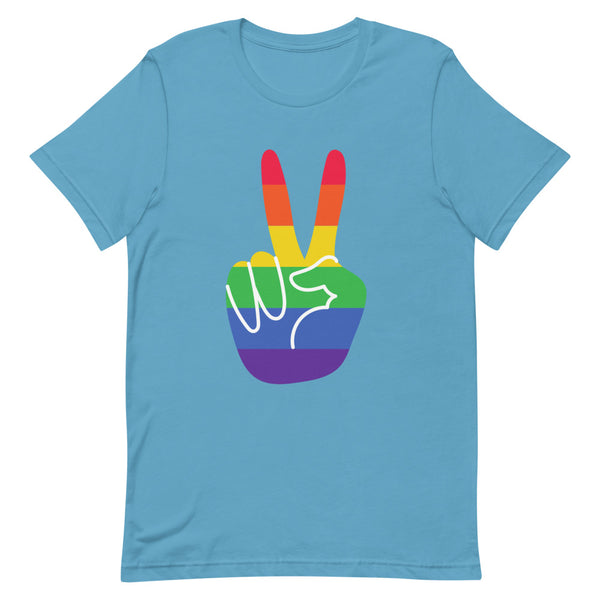 Gay Pride T-shirt featuring a rainbow peace sign, worn by a smiling person with shoulder-length dark hair in a cozy living room.