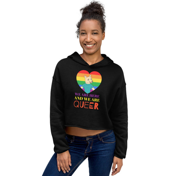 Front view of a model wearing a black cropped hoodie reading “WE ARE HERE AND WE ARE QUEER”