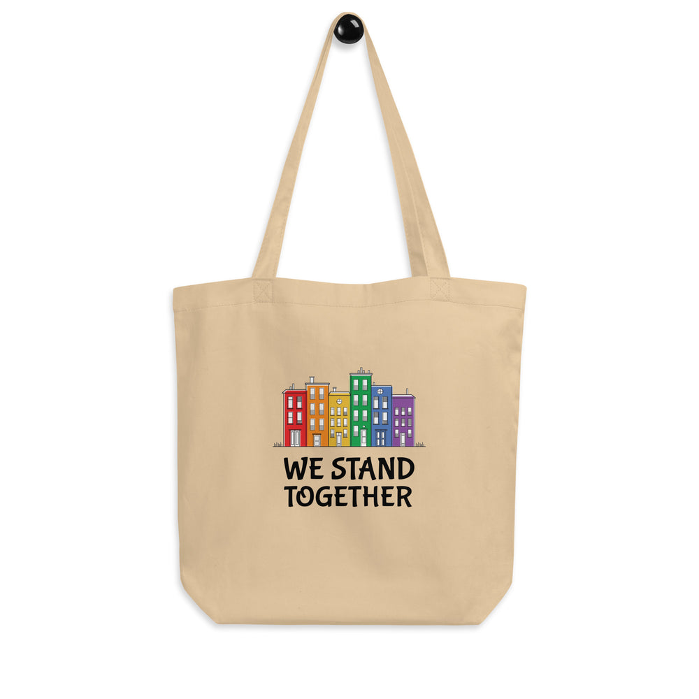 Front-facing beige tote bag with colorful row houses and “WE STAND TOGETHER” text
