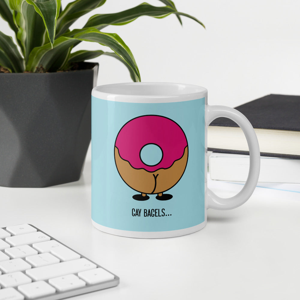 White mug with a pink-frosted doughnut graphic and the words “GAY BAGELS…”