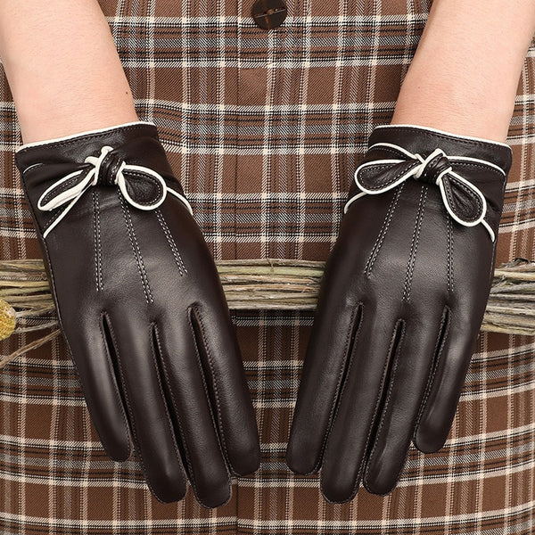 Pair of dark brown leather gloves with white-trimmed bows, worn over plaid fabric