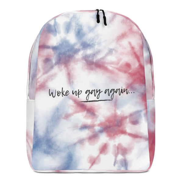Front view of a pink, blue, and white tie-dye backpack reading “Woke up gay again...”
