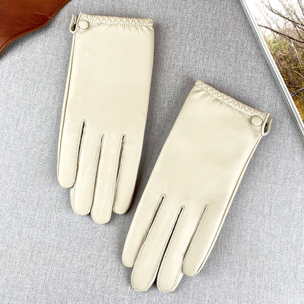 Pair of cream leather gloves laid flat on gray fabric, showing stitched cuffs and finger seams