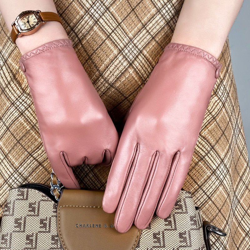 Close-up of pink leather gloves worn over a plaid outfit beside a watch and handbag