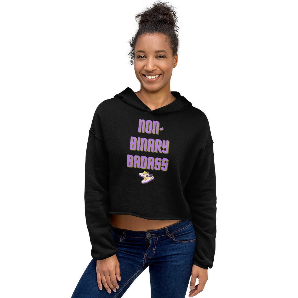 Model wearing a black cropped hoodie reading “NON-BINARY BADASS” with a sneaker graphic