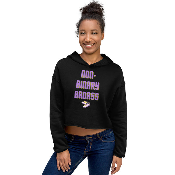 Model wearing a black cropped hoodie reading “NON-BINARY BADASS” with a sneaker graphic