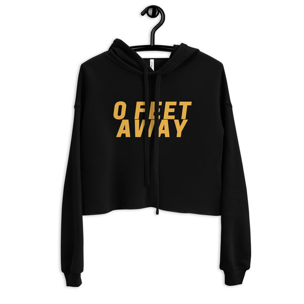 Front view of a black cropped hoodie with gold “0 FEET AWAY” lettering on a hanger