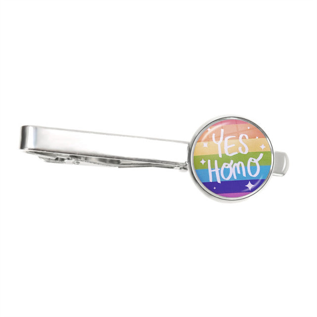 Silver tie clip with a round rainbow badge reading “Yes Homo”